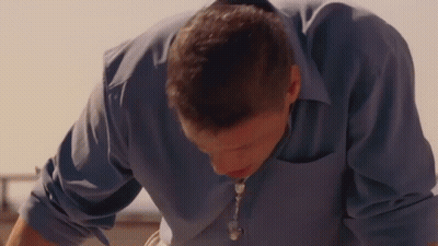 Man In Blue Shirt And Necklace Looking Down GIF
