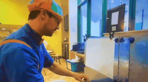 Man In Blue Shirt And Orange Hat Working In Kitchen GIF