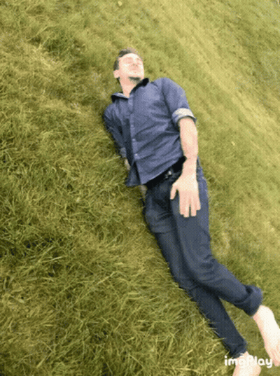 Man In Blue Shirt And Tie Laying On Grassy Hill GIF