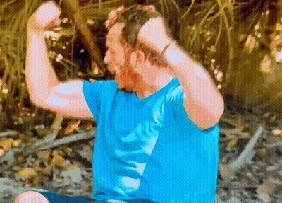 Man In Blue Shirt Flexing Muscles Sitting On Ground GIF