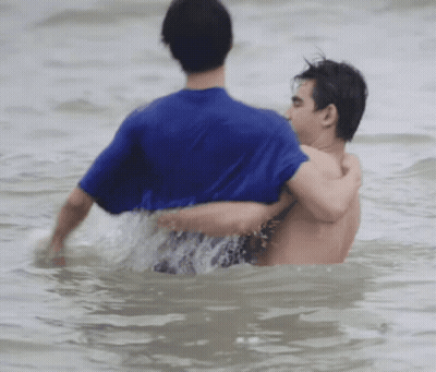Man In Blue Shirt Helping Another Out Of Water GIF