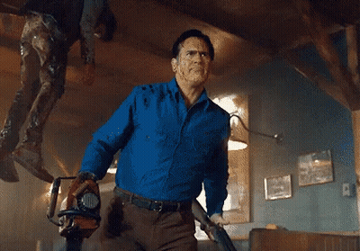 Man In Blue Shirt Holding Chainsaw And Gun GIF