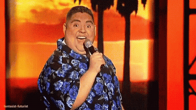 Man In Blue Shirt Holding Microphone Smiling On Stage GIF