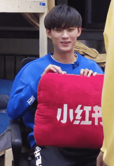 Man In Blue Shirt Holding Red Pillow With Chinese Characters GIF