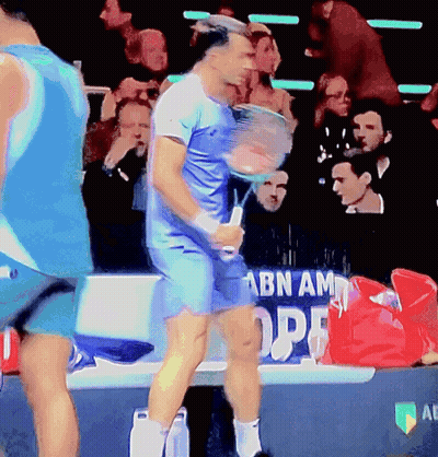 Man In Blue Shirt Holding Tennis Racquet In Front Of ABN AM OPE Banner GIF