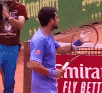 Man In Blue Shirt Holding Tennis Racquet In Front Of Emirates Fly Bett Sign GIF