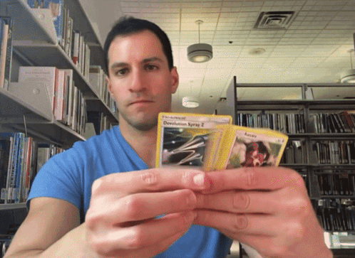 Man In Blue Shirt Holding Two Pokemon Cards Including Devolution Spray GIF