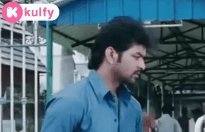 Man In Blue Shirt In Front Of Building With Kulfy Sign GIF