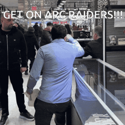 Man In Blue Shirt In Front Of Get On Arc Raiders Display Case GIF