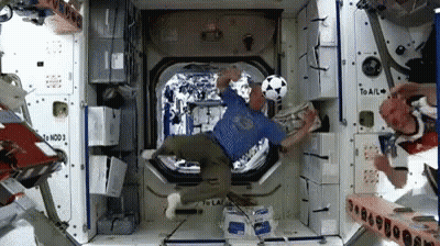 Man In Blue Shirt Kicking Soccer Ball In Space Station GIF
