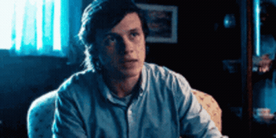 Man In Blue Shirt Looking At Camera In Dark Room GIF