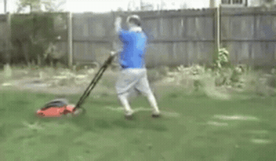 Man In Blue Shirt Mowing Lawn With Red Lawn Mower GIF