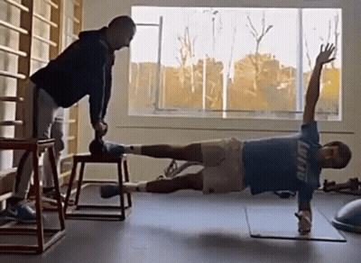 Man In Blue Shirt Planking, Another Holding Dumbbell GIF