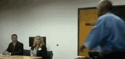 Man In Blue Shirt Presenting To Group At Table GIF
