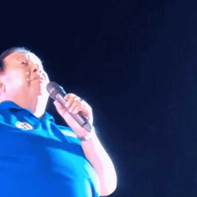 Man In Blue Shirt Singing Into Microphone With Letter S GIF