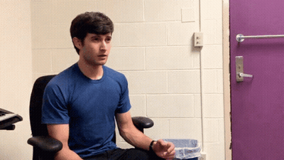 Man In Blue Shirt Sitting In Front Of Purple Door GIF