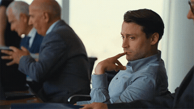 Man In Blue Shirt Sitting With Hand On Chin GIF