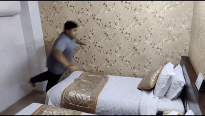 Man In Blue Shirt Standing In Front Of Bed GIF