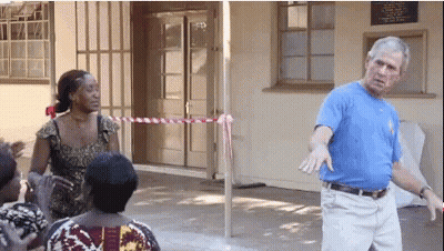 Man In Blue Shirt Standing In Front Of Building With Sign GIF