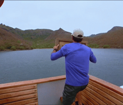Man In Blue Shirt Standing On Boat Holding Box GIF