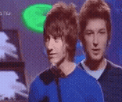 Man In Blue Shirt Talking Into Microphone With Two Men Looking On GIF