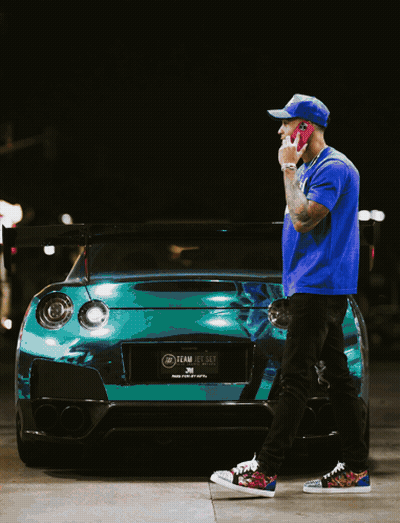 Man In Blue Shirt Talking On Cell Phone In Front Of Green Car GIF