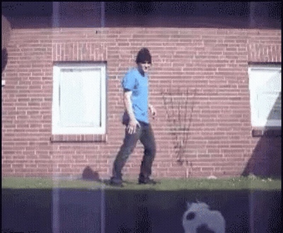 Man In Blue Shirt Walking In Front Of Brick Wall GIF