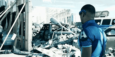Man In Blue Shirt With Letter A In Front Of Destroyed Building GIF