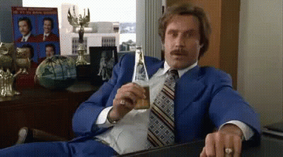 Man In Blue Suit Holding Beer At Desk GIF