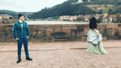 Man In Blue Suit Next To Woman In Green Dress Mayward On Sidewalk GIF