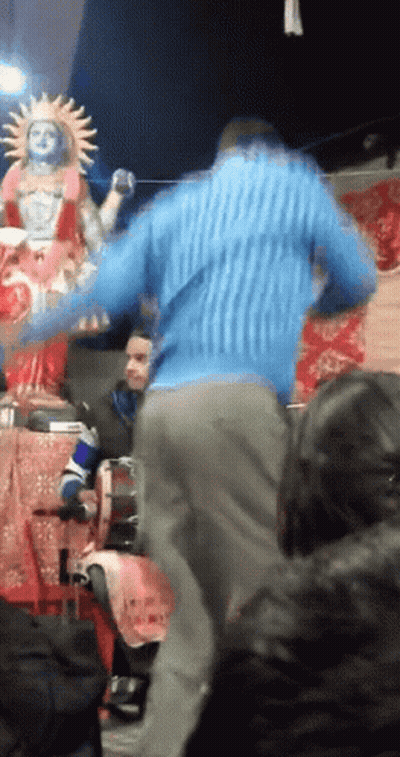Man In Blue Sweater Dancing In Front Of Sun Statue GIF