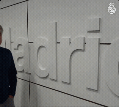 Man In Blue Sweater In Front Of Wall Saying Madrid GIF