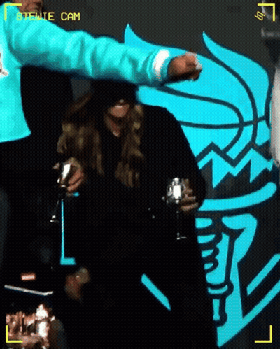 Man In Blue Sweatshirt Holds Glass In Front Of Stewie Cam Logo GIF