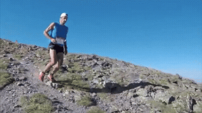 Man in Blue Tank Top Running Up Rocky Hill