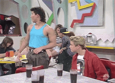 Man In Blue Tank Top Talking To Man In Red Jacket In Diner GIF