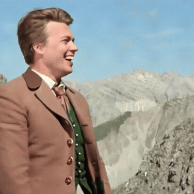 Man In Brown Coat In Front Of Mountains GIF