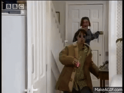 Man In Brown Coat Walking Down Hallway With Woman In Sunglasses GIF