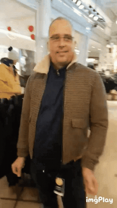 Man In Brown Jacket And Glasses Standing In Store GIF