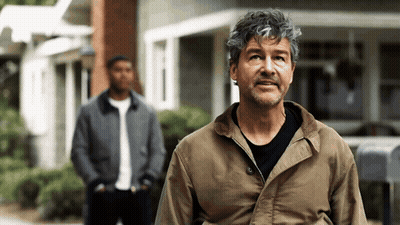 Man In Brown Jacket Standing In Front Of Building GIF