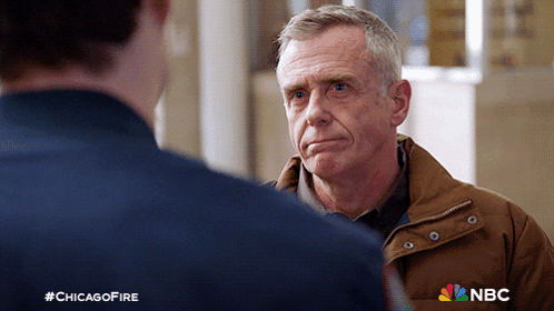 Man In Brown Jacket Talking To Man In Blue Shirt NBC Logo GIF