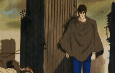 Man In Brown Poncho Standing In Front Of Building GIF