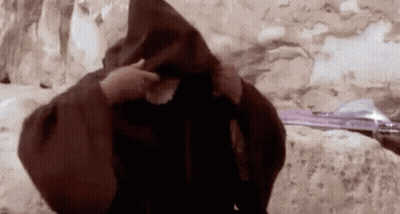 Man In Brown Robe Standing By Stone Wall GIF