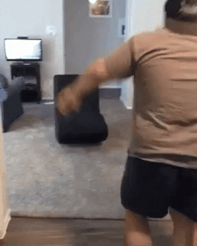 Man In Brown Shirt Standing In Living Room With Chair GIF