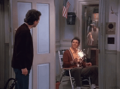 Man In Brown Sweater Next To Man Holding Sparkler GIF
