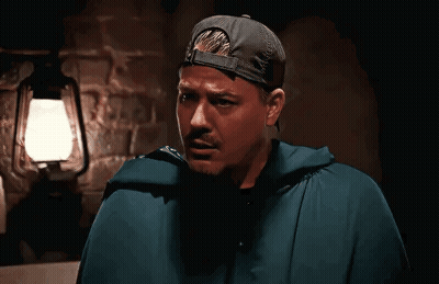 Man In Cape And Baseball Cap In Front Of Lantern GIF
