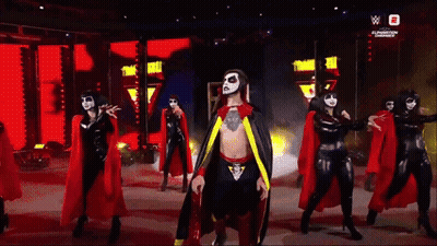 Man In Cape Surrounded By Women In Black And Red GIF