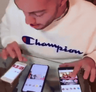 Man In Champion Sweatshirt Looking At Two Phones GIF
