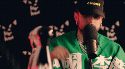 Man In Chomp Hat And Green Shirt Singing Into Microphone GIF