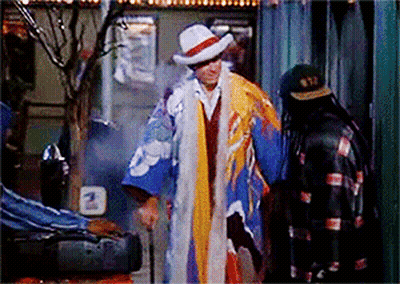 Man In Colorful Coat And Hat Next To Man In Black Jacket GIF