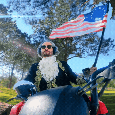 Man In Costume Holding American Flag Riding Golf Cart GIF